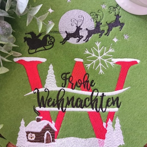 May include: A green Christmas placemat with a festive design. The placemat features a large red letter "W" with the words "Frohe Weihnachten" in black script. A silhouette of Santa's sleigh and reindeer is above the letter.