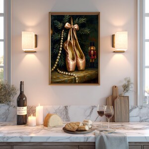 May include: A framed painting depicts ballet pointe shoes hanging from a bow, with a pearl necklace and a toy nutcracker. The painting is set against a backdrop of evergreen branches. The scene is in a kitchen with a marble countertop.