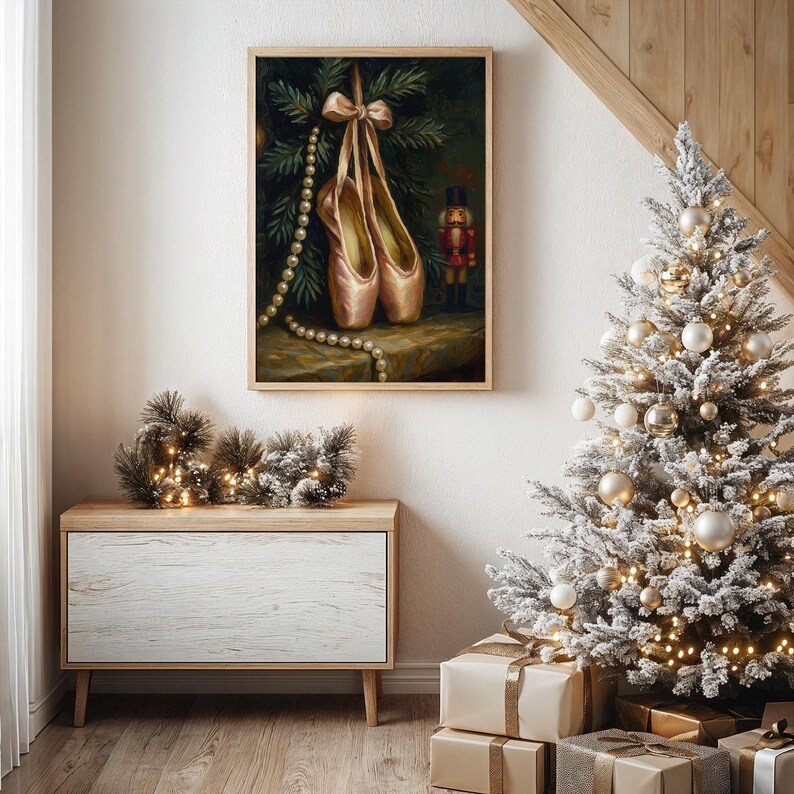May include: A framed painting depicts ballet pointe shoes hanging from a bow, with a pearl necklace and a nutcracker. The artwork is set against a backdrop of evergreen branches, evoking a holiday theme. A Christmas tree and wrapped gifts are in the foreground.