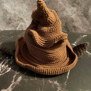 May include: A brown crocheted Sorting Hat, a popular accessory from the Harry Potter series. The hat has a pointed top and a wide brim.