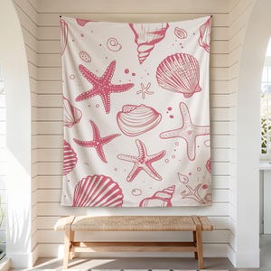 May include: A white tapestry with a repeating pattern of pink seashells and starfish. The design includes various shell shapes and starfish in different sizes, creating a beach-themed aesthetic. The tapestry is hanging on a white wall.