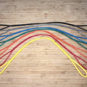 May include: A collection of colorful braided ropes in various hues, including black, gray, blue, green, orange, red, and yellow. Each rope is looped at both ends, arranged on a wooden surface.