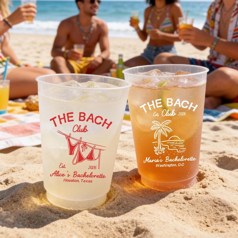 May include: Two clear plastic cups filled with drinks, sitting on a sandy beach. The cups have the text "THE BACH Club" printed in red. One cup says "Alice's Bachelorette, Houston, Texas". The other says "Maria's Bachelorette, Washington, D.C."