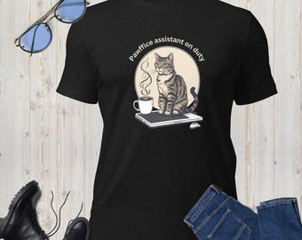 Op de afbeelding: Zwart T-shirt met een afbeelding van een tabby kat op een toetsenbord, een kopje koffie en de tekst "Pawffice assistant on duty". Het shirt wordt gecombineerd met een blauwe jeans, zwarte laarzen en een zonnebril.