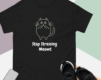May include: Black t-shirt featuring a white outline drawing of a surprised cat. The text "Stop Stressing Meowt" is below the cat illustration. Black sneakers and a smartphone are in the foreground.