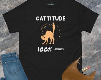 May include: Black t-shirt with the word "CATTITUDE" above a cartoon cat illustration. The cat is orange and arched, with a dotted circle around it. Below the cat is "100%" and a loading bar graphic.