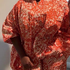 May include: A vibrant red and white patterned kimono-style outfit. The ensemble features a loose-fitting top and matching pants, both adorned with a bold, abstract design. The outfit is complemented by matching earrings, creating a cohesive and stylish look.