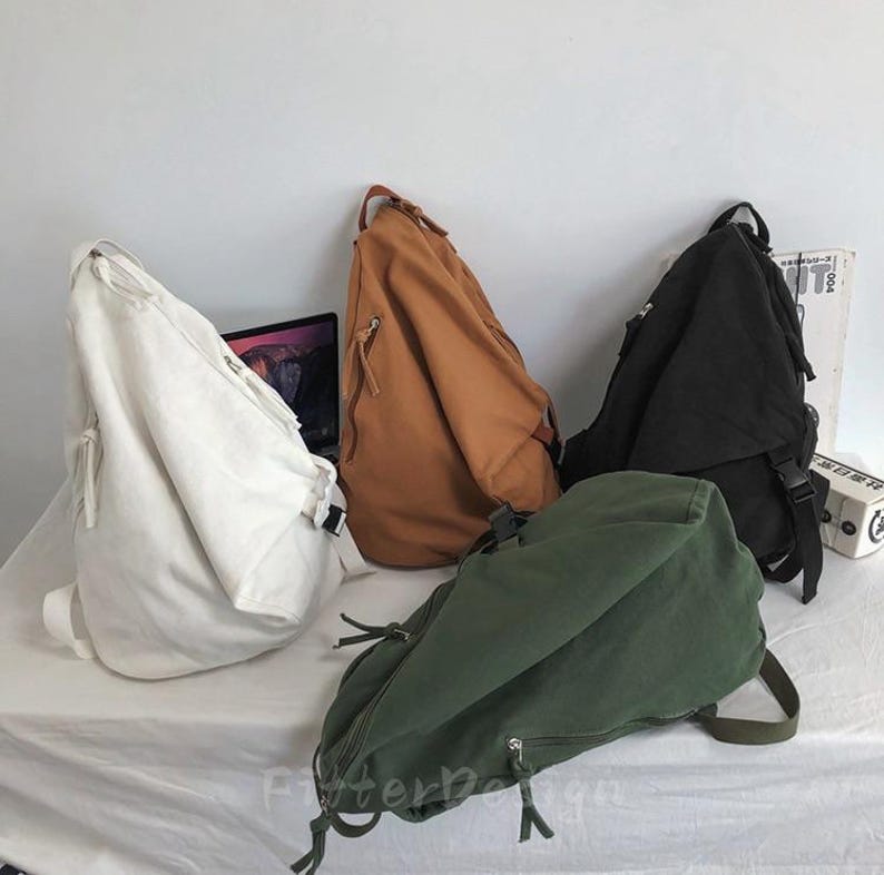 Puede incluir: Cuatro mochilas bandoleras de lona en blanco, marr&oacute;n, negro y verde oliva. Cada bolsa tiene una sola correa para el hombro, un compartimento principal con cremallera y correas ajustables. Las bolsas se muestran sobre un fondo blanco.