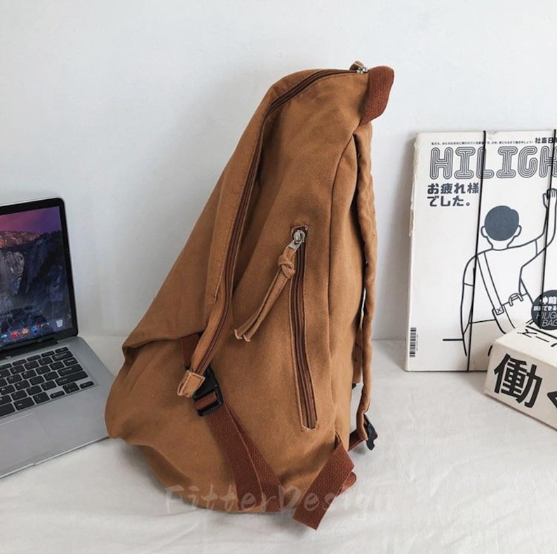 Puede incluir: Una mochila de lona marr&oacute;n con m&uacute;ltiples compartimentos con cremallera y correas ajustables. La mochila tiene un asa superior y un cierre de hebilla. Un port&aacute;til y un libro est&aacute;n en el fondo.
