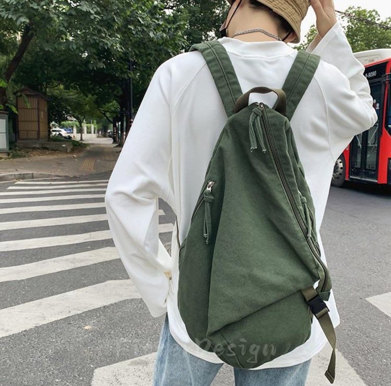 Puede incluir: Mochila de lona verde oliva con cremallera diagonal y correas ajustables. La mochila tiene un peque&ntilde;o bolsillo con cremallera en la parte delantera y un cierre de hebilla. La bolsa se lleva sobre el hombro.