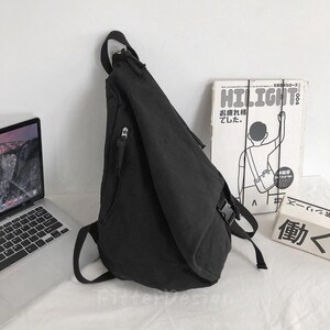 Puede incluir: Bandolera negra con una sola correa para el hombro y m&uacute;ltiples compartimentos con cremallera. La bolsa est&aacute; hecha de una tela duradera y tiene un cierre de hebilla. Un port&aacute;til y un libro con texto japon&eacute;s est&aacute;n en el fondo.