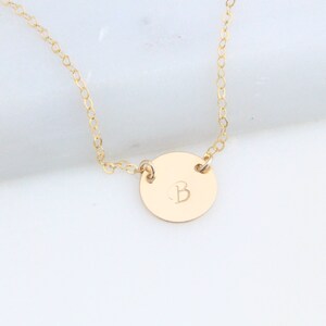 May include: A gold chain necklace with a round pendant featuring the letter "B" engraved on it.