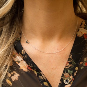 May include: A silver necklace with a crescent moon pendant. The necklace is worn by a person with long blonde hair and a floral patterned shirt.