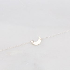 May include: A delicate silver chain necklace with a crescent moon pendant.