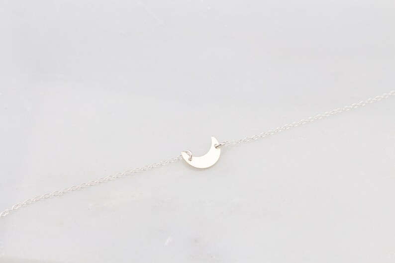 May include: A delicate silver chain necklace with a crescent moon pendant.