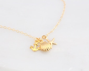 May include: Gold necklace with a seashell, anchor, and starfish charm. The necklace is on a white background.