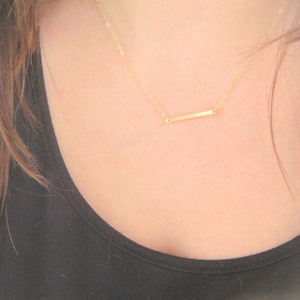 May include: A delicate gold necklace with a thin, horizontal bar pendant.