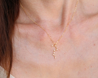 May include: A gold chain necklace with a delicate pendant featuring a constellation design with small white stones.