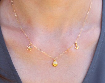 May include: A gold chain necklace with three charms: a seashell, a starfish, and an anchor.