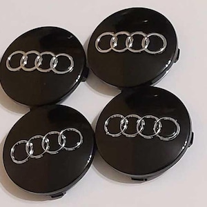 Peut inclure: Quatre enjoliveurs de roue noirs avec le logo Audi argenté. Les enjoliveurs sont ronds et brillants, avec un emblème argenté en relief de quatre anneaux entrelacés. Ces enjoliveurs sont probablement pour une voiture.