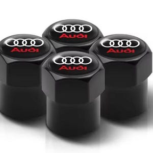 Könnte beinhalten: Vier schwarze Reifenventilkappen mit dem Audi-Logo in Weiß und Rot. Die Kappen haben eine sechseckige Form und sind auf weißem Hintergrund angeordnet.