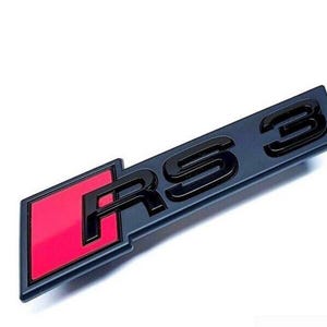 Può includere: Un emblema RS3 grigio scuro con scritte nere e un quadrato rosso. L'emblema rettangolare è angolato, con le lettere "RS3" ben visibili. Lo sfondo è bianco.