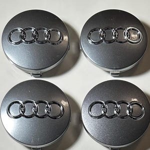Peut inclure: Quatre enjoliveurs de roue Audi argentés. Chaque enjoliveur présente le logo Audi, composé de quatre anneaux entrelacés en finition chromée. Les enjoliveurs ont un éclat métallique et une forme circulaire.