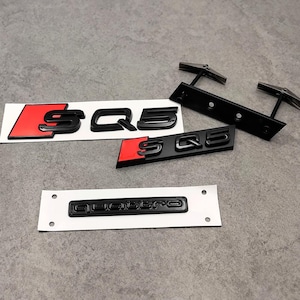 Peut inclure: Emblèmes de voiture SQ5 noirs avec des accents rouges et un emblème Quattro noir. Les emblèmes SQ5 sont sur des cartes de support blanches. Sont également inclus des supports de montage en métal noir.