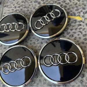 Peut inclure: Quatre enjoliveurs de roue de voiture noirs et argentés avec le logo Audi. Les enjoliveurs ont une finition noire brillante avec une bordure argentée et l'emblème des anneaux entrelacés.