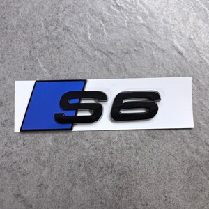 Peut inclure: Un emblème rectangulaire présentant un parallélogramme bleu sur le côté gauche et le texte noir S6 sur la droite. L'emblème est monté sur un support rectangulaire blanc. Le design se compose d'une forme bleue audacieuse à côté du caractère S6.