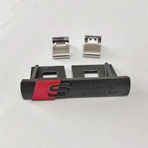 Peut inclure: Emblème S line noir et rouge avec deux clips argentés. L'emblème présente le texte "S line" et un design "S" rouge. Les clips sont rectangulaires et métalliques.