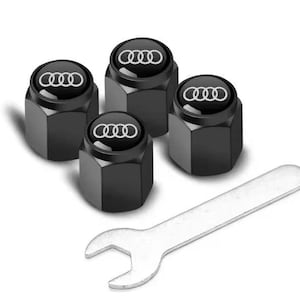 Könnte beinhalten: Satz von vier schwarzen Reifenventilkappen mit dem weißen Audi-Logo. Ein silberner Schraubenschlüssel ist enthalten. Die Kappen haben eine sechseckige Form. Kfz-Zubehör.