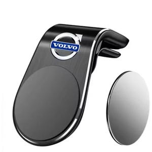 May include: A black car phone mount with a silver trim and a circular magnetic base. The mount features the Volvo logo in blue and white. An additional silver magnetic disc is included.