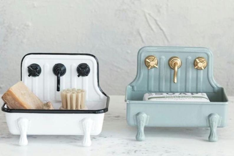 White farmhouse sink soap dish with black rim, faucets and knobs pictured on the left. On the right is a light blue farmhouse sink dish with gold faucet and knobs.