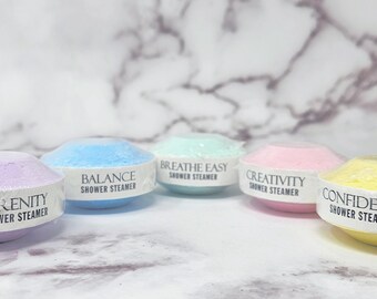 May include: Five round shower steamers in different colors and scents. The scents are Serenity, Balance, Breathe Easy, Creativity, and Confidence.