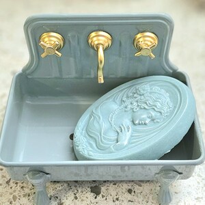 Grey Blue Farmhouse Sink Fish with gold faucet and knobs. Blue cameo soap is sitting in dish.