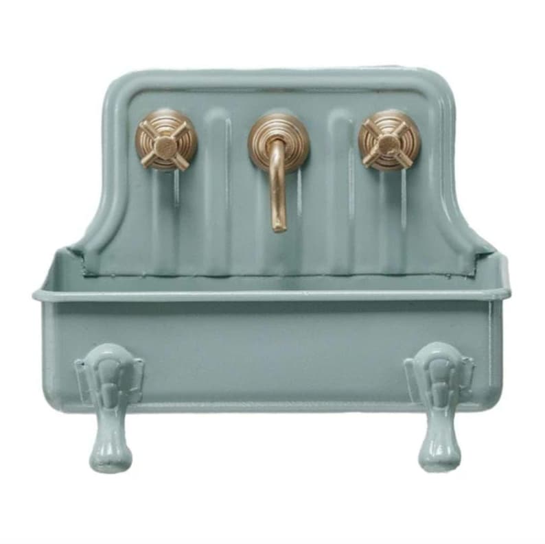Op de afbeelding: Een lichtblauwe metalen gootsteen met een decoratief ontwerp en drie gouden kranen. De gootsteen heeft twee decoratieve poten.
