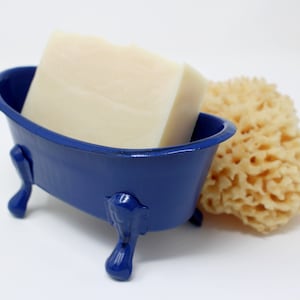 May include: A blue ceramic bathtub-shaped soap dish with a white bar of soap inside. A natural loofah sponge is next to the soap dish.