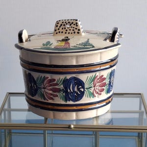 Peut inclure: Une enseigne en bois avec le texte "ENTREZ, C'est ouvert" et un seau décoratif en céramique avec un motif floral, posé sur une boîte d'exposition en verre avec un cadre doré. L'enseigne a un logo dans le coin supérieur gauche.