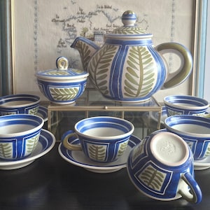 Peut inclure: Service à thé en céramique bleu et blanc, comprenant une théière, un sucrier et six tasses avec soucoupes. L'ensemble présente un motif de feuilles vertes. L'ensemble est présenté sur une surface noire.