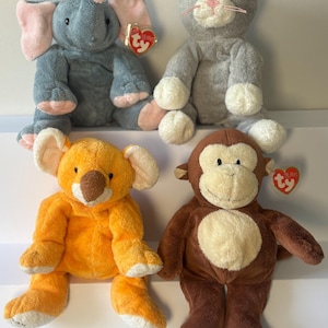 以下が含まれることがあります： 象、猫、コアラ、猿の4つのぬいぐるみ。象はグレーにピンクのアクセント、猫は白い足のグレー、コアラはオレンジ、猿は茶色です。各おもちゃにはTyタグが付いています。