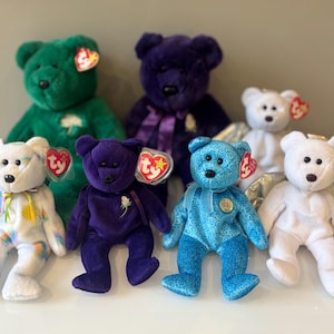 Può includere: Una collezione di orsacchiotti di peluche colorati. Gli orsi sono in vari colori, tra cui verde, viola, blu e bianco. Ogni orso ha un'etichetta attaccata. Alcuni orsi hanno nastri o altri elementi decorativi.