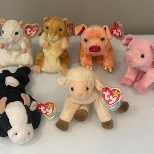 Peut inclure: Plusieurs peluches d'animaux : une souris blanche, un hamster brun, deux cochons orange et rose, une vache noire et blanche et un agneau crème. Chaque jouet est accompagné d'une étiquette en forme de cœur.