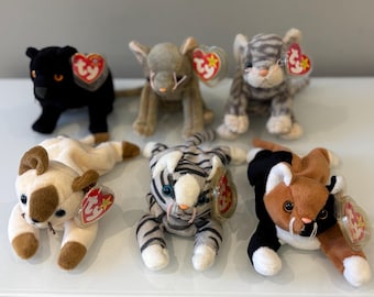 Puede incluir: Una colección de seis peluches Beanie Baby con varios diseños de animales. Los peluches incluyen una pantera negra, un gato gris, un tigre, un gato siamés, un tigre y un gato calicó. Cada juguete tiene una etiqueta en forma de corazón Ty.