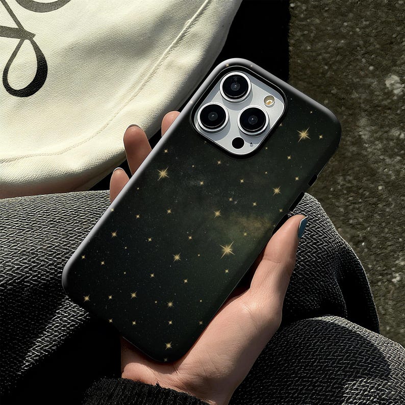 May include: Black smartphone case with a starry night design. The case features a dark background with numerous small, golden stars scattered across the surface. The phone's camera lenses are visible at the top.