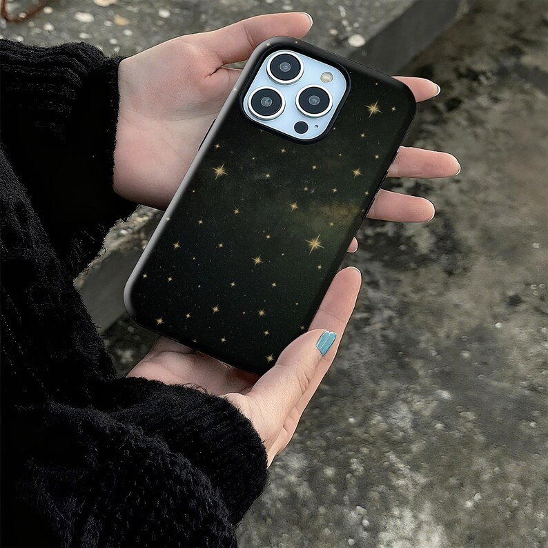 May include: Black phone case with a starry night design. The case features a dark background with numerous gold stars scattered across the surface. The phone case has a black border and a camera cutout.