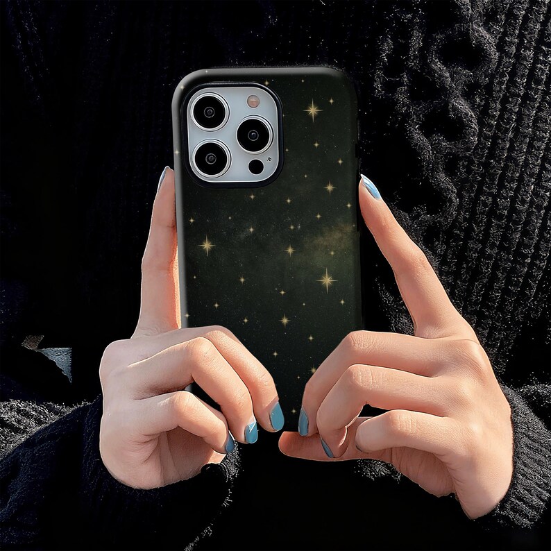 May include: A black phone case with a starry night design. The case features a dark background with numerous small, golden stars scattered across it. The phone case has a black border and cutouts for the phone's camera.