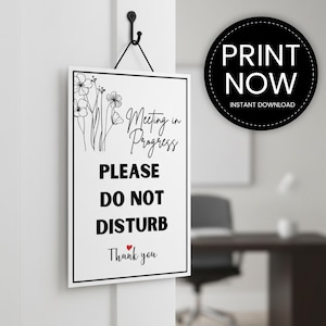 Op de afbeelding: Een wit rechthoekig bord met een zwarte rand, hangend aan een zwarte haak. Het bord leest "Meeting in Progress, PLEASE DO NOT DISTURB, Thank you" in zwarte tekst. Bloemenlijntekeningen versieren de linkerbovenhoek. Een zwarte cirkel met witte tekst "PRINT NOW, INSTANT DOWNLOAD" staat rechts.