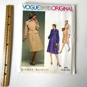 May include: A vintage Vogue Paris Original sewing pattern for a dress by Pierre Balmain. The pattern number is 1498. The pattern shows three different views of the dress, one in beige, one in purple, and one in brown.