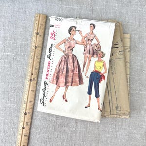 Può includere: Modello di cucito stampato Simplicity vintage con illustrazioni di abbigliamento femminile. Il pacchetto del modello mostra un abito a righe, un completo con pantaloncini e pantaloni capri. Un righello di legno è visibile sul lato sinistro dell'immagine.